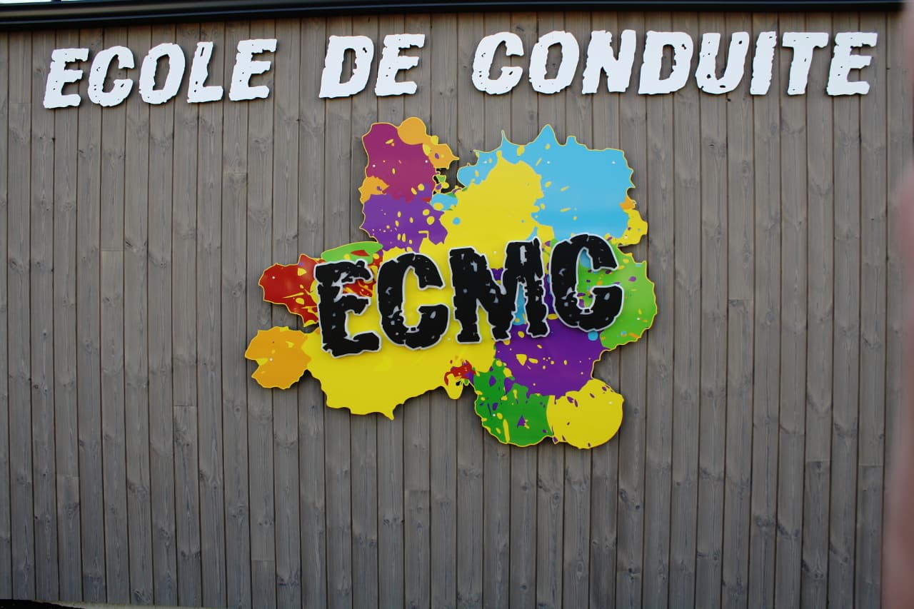 Enseigne colorée ECMC — École de Conduite — sur la façade en bois du centre